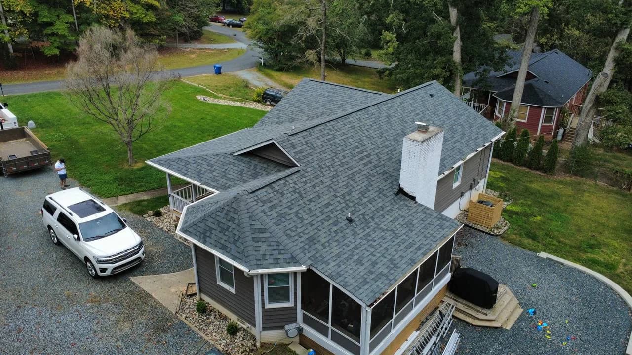 Aerial view of completed asphalt shingle roof replacement on a gray home with screened porch