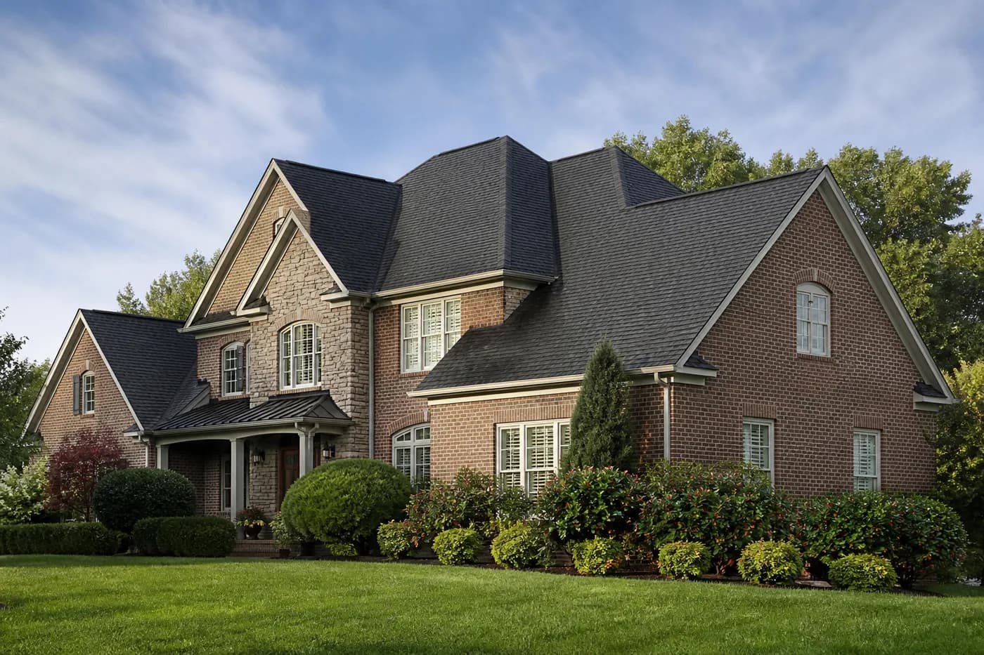 Roof-dominant upscale Stallings NC brick-and-stone home with a coherent charcoal architectural shingle roof after rain
