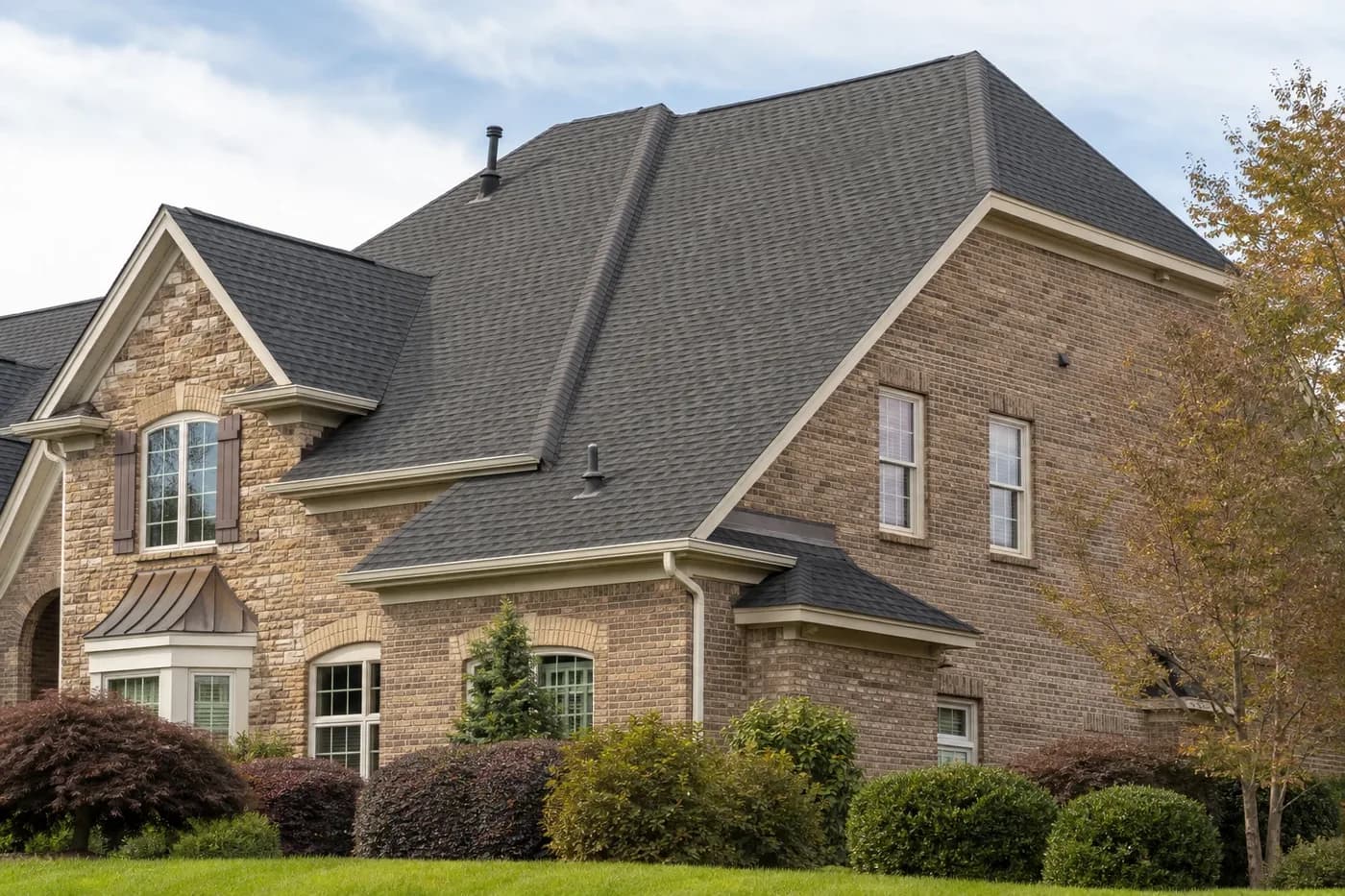 Roof-dominant upscale Waxhaw NC brick-and-stone home with coherent roof-to-wall transitions and charcoal architectural shingles