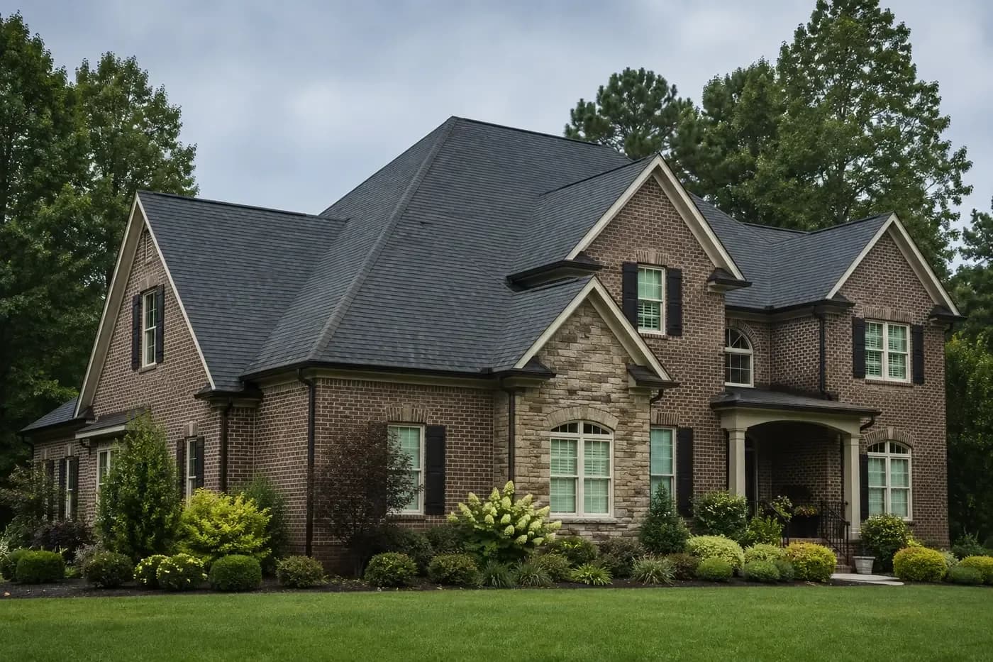 Roof-dominant upscale Monroe NC brick-and-stone home with a coherent charcoal architectural shingle roof