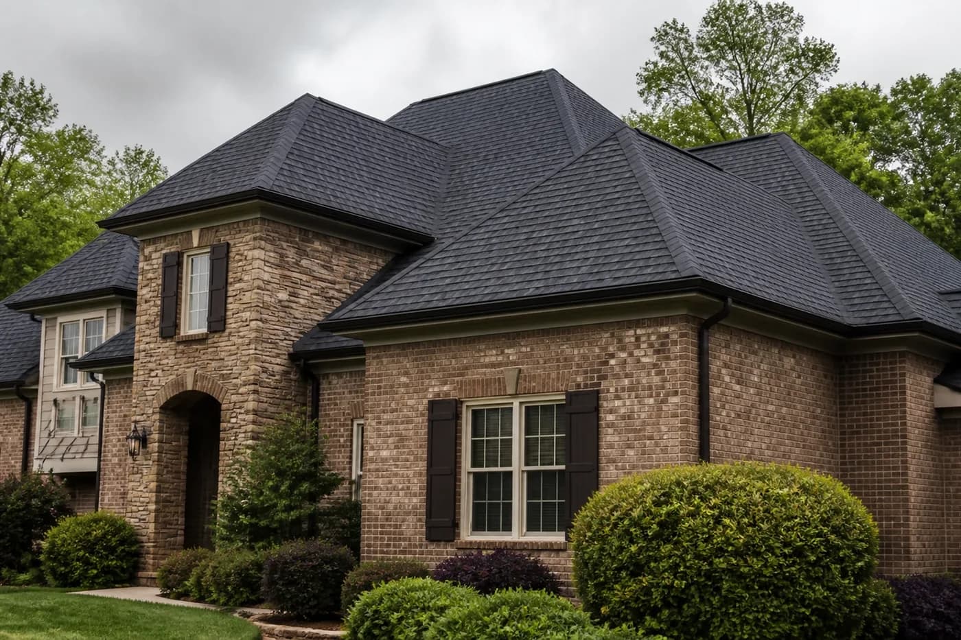 Roof-dominant upscale Matthews NC brick-and-stone home with coherent charcoal hip and ridge cap shingles